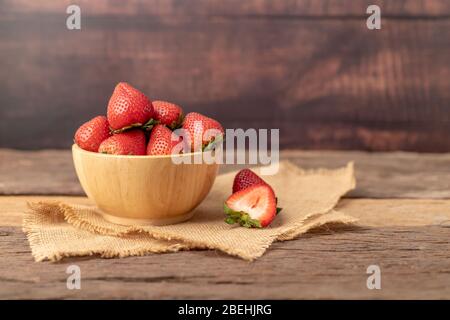 Strawberries are in a wooden bowl on a brown sack placed on the table. Stock Photo