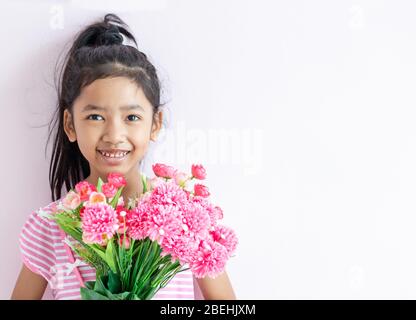 Portrait of an Asian little girl wearing a pink and white striped dress. The child holding bouquet flowers with smiling and happy. Select the focus an Stock Photo