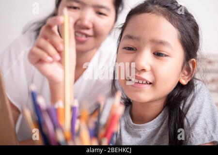 Asian little girl picking a gold color pencil with mother. Children learning with parent to prepare for going to school. Stock Photo