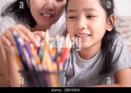 Asian little girl picking a color pencil with mom. Mother and daughter share their vacations. Children learning painting with parent. Stock Photo