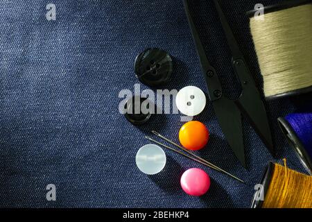 Needle and threads against plastic button and thread cutting scissors on jeans fabric. Top view and copy space for text. Concept of tailor or Designer Stock Photo