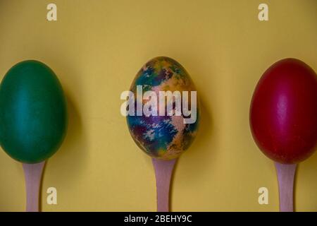 Three colorful eggs in wooden spoons isolated on yellow background, multicolored eggs, Easter tradition, celebration concept Stock Photo