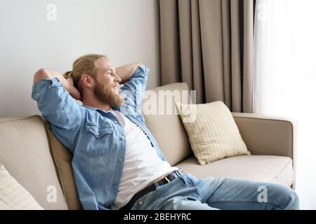 Smiling relaxed young man lounge on comfortable sofa looking away. Stock Photo
