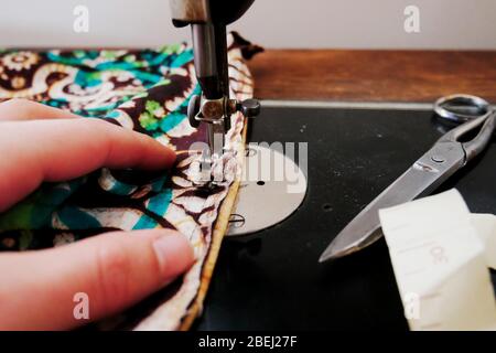 Close-up of person using vintage sewing machine with fabric, scissors and measuring tape Stock Photo