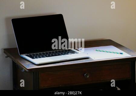 Laptop, paper and pencil on wooden desk with plain background Stock Photo