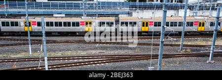 Criss-crossing heavy rail train tracks on gravel in the city with a moving commuter train running across the frame. Brisbane, Roma Street station. Stock Photo