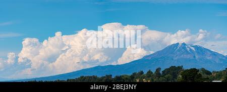 large formation clouds next to the top of calbuco volcano on a sunny day, with its hills covered with native forest Stock Photo