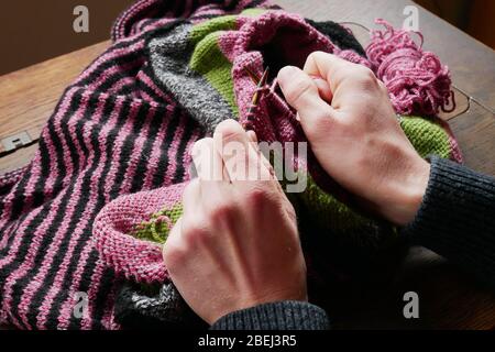 Close-up view of a man knitting on an old wooden desk Stock Photo