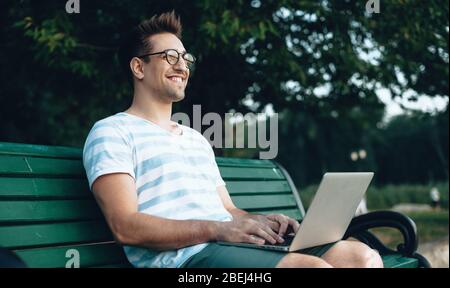 Caucasian freelancer with eyeglasses working at the computer on a bench in park Stock Photo