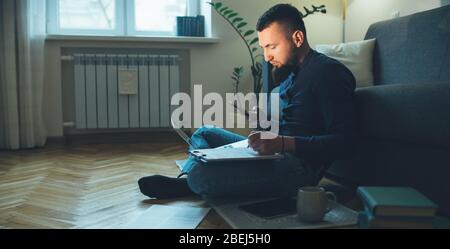 Side view portrait of caucasian man with beard chatting with somebody the floor using a laptop while working with some documents Stock Photo