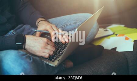 Caucasian businessman working at home with a laptop and some documents sitting on the sofa Stock Photo