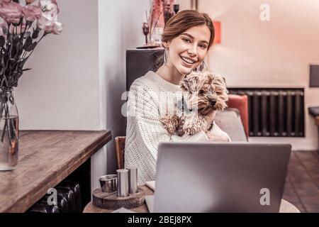 Smiling beautiful woman working on laptop with her pet in cafe Stock Photo