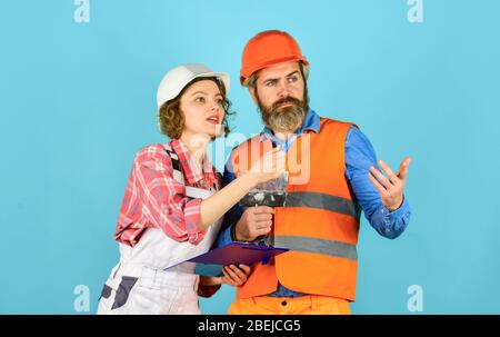 Plastering works. Couple look documents. Woman and man safety hard hat. Couple planning changes renovation apartment. Renovation concept. According to plan. Discussing renovation with contractor. Stock Photo