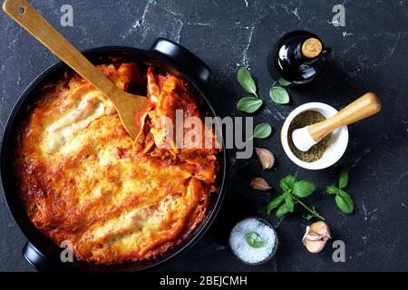 Traditional italian cannelloni pasta stuffed with bolognese sauce and mozzarella cheese on top on a black baking dish on dark concrete background with Stock Photo