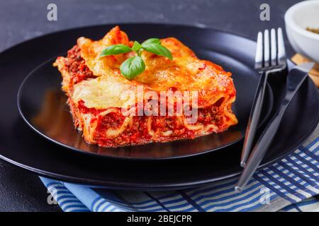 Restaurant portion of stuffed pasta manicotti with beef bolognese sauce and mozzarella cheese on top on a black plate on dark concrete background, cut Stock Photo