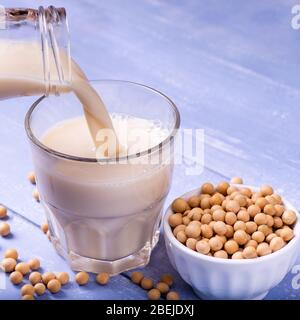 on the table in light blue wood, yellow soy beans and soy milk in the glass in the foreground Stock Photo