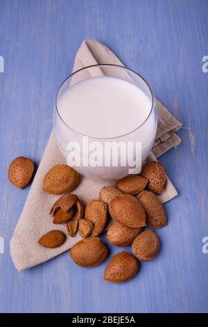 almond milk in the glass, and on the table colored with blue, almonds, with and without shell Stock Photo