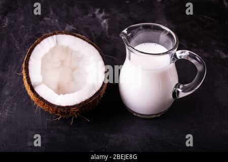 front view, half coconut and coconut milk in glass carafe, on dark background Stock Photo