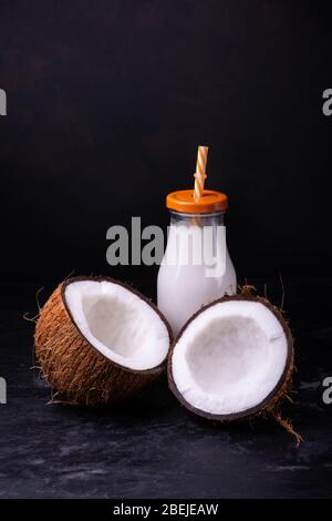 front view, two halves coconut and coconut milk in the glass bottle, on dark background Stock Photo