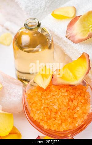 Wellness center. In the foreground orange-flavored bath salts, transparent glass bottle with perfumed essential oil, white towels, and rose petals. Stock Photo