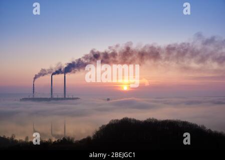 Colorful blue and pink sky with bright rising sun at thermoelectric power plant. Thermal chimneys producing dense smoke with toxic gases into atmosphere. Concept of ecology and environmental pollution Stock Photo
