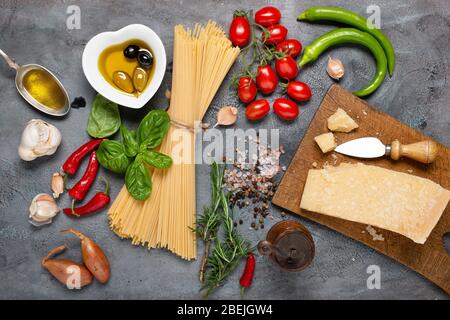 top view, on a dark gray rustic background, Italian spaghetti with olive oil, seasoned cheese, bunch of tomatoes, various vegetables and spices Stock Photo