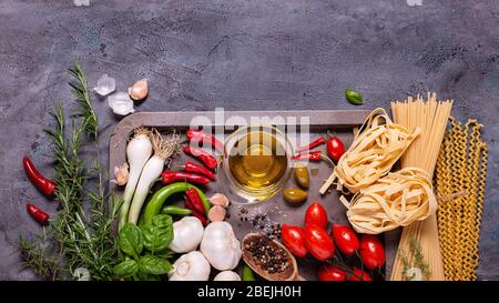 top view, on a rustic dark gray background, raw pasta and traditional Italian ingredients with olive oil, various vegetables and spices Stock Photo