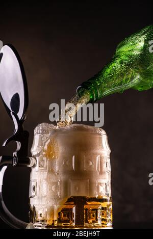 fresh and frothy beer poured from the bottle into the glass mug on the dark background Stock Photo