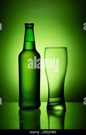 a bottle of beer with condensation and an empty glass isolated on the green background Stock Photo