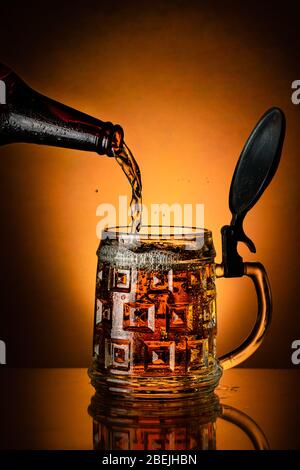 fresh beer poured from the bottle into the glass mug on the golden background Stock Photo