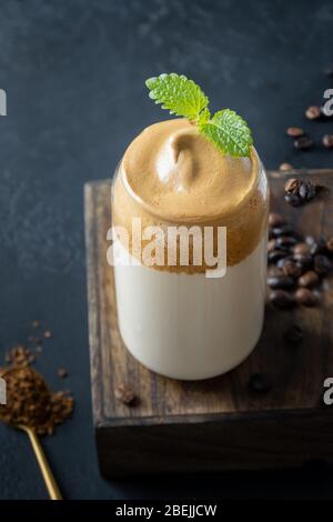 Dalgona frothy coffee in glass on dark. Trend korean drink latte espresso with foam of instant coffee. Vertical shot. Stock Photo
