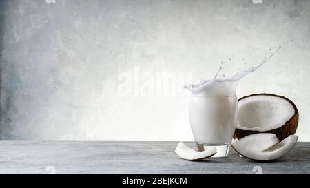 vegetable drink made from coconut in the glass and parts of coconut, on a rustic gray background. Empty space for text Stock Photo
