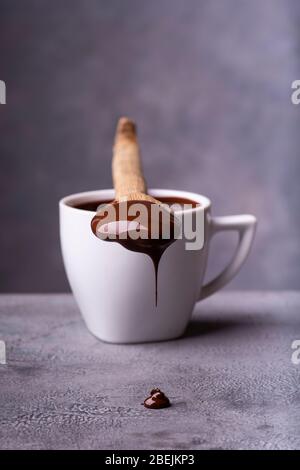 from the wooden spoon, smeared with melted chocolate, drops of chocolate fall on the gray worktop Stock Photo