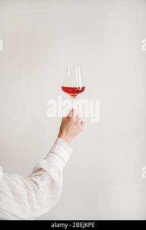Womans hand holding glass of rose wine over white wall Stock Photo