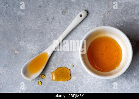 organic chestnut honey. white ceramic vase and spoon with dripping honey lying on the gray structure. Stock Photo