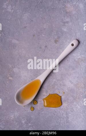 organic chestnut honey is poured from the white ceramic spoon isolated on gray texture with top view. Stock Photo