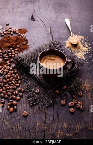 On the raw and dark wooden table, a cup of coffee with a spoonful of brown sugar and roasted coffee beans. Stock Photo