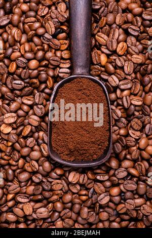 background with roasted coffee beans with a wooden spoon full of ground coffee in the middle Stock Photo