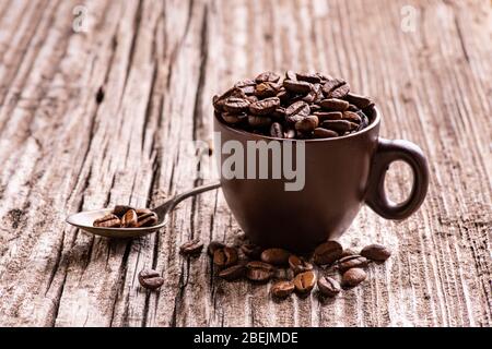 in the foreground, on worn wood, roasted coffee beans in the brown ceramic cup. Stock Photo