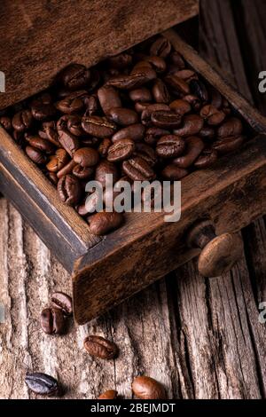 in the foreground, on worn wood, a pile of roasted coffee beans in the drawer of an old wooden grinder Stock Photo