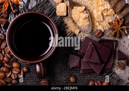 seen from above. In the foreground, a cup of black coffee, a spoon with brown sugar, some pieces of dark chocolate and star anise. Stock Photo
