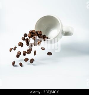 isolated from the white background, a cup of coffee suspended in the air from which a cascade of roasted coffee beans flows Stock Photo