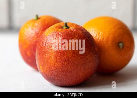 Three Sicilian blood red oranges isolated laying on the tablecloth on white brick wall background Stock Photo