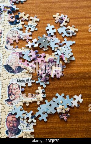 Jigsaw pieces and a partially completed jigsaw on a wooden table. Stock Photo