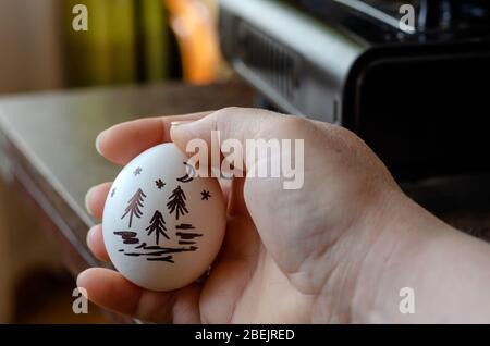 Drawing on a chicken egg. The hand holds a raw egg with a landscape picture on the shell. Close-up. Selective focus. Stock Photo