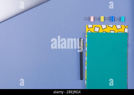 Pile of bright notebooks , laptop and stationary on blue desk top. Copy space. Free space.  Stock Photo