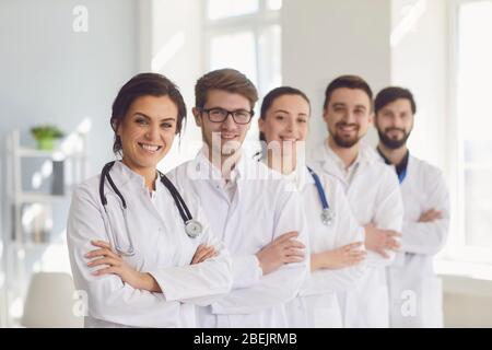 A group of confident practicing doctors in white coats are smiling against the backdrop of the clinic. Stock Photo