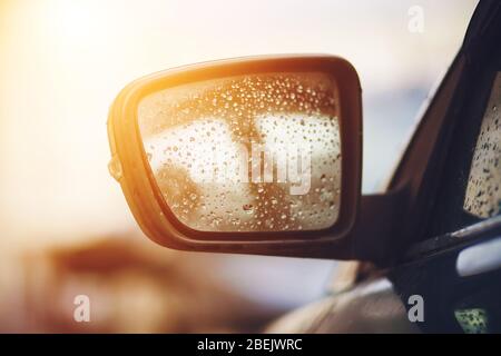 The rearview mirror on a passenger car is wet from raindrops and is illuminated by sunlight. Stock Photo