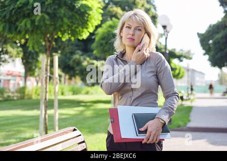 Middle-aged confident business woman talking on smartphone, portrait of successful female in city Stock Photo
