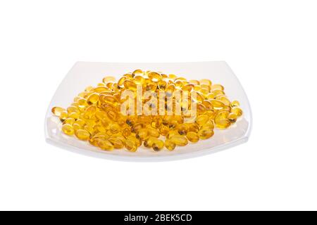Softgels of Omega-3 on a white plate. Vitamins fish oil on a white background. Yellow capsules with medicine. Meal replacement. Medical medicament of Stock Photo